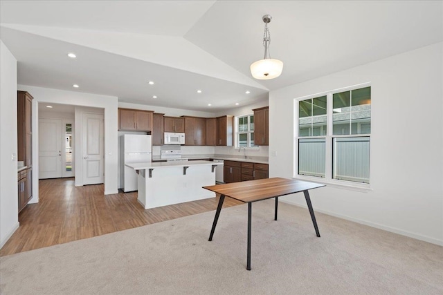kitchen with a sink, white appliances, recessed lighting, light countertops, and a kitchen island