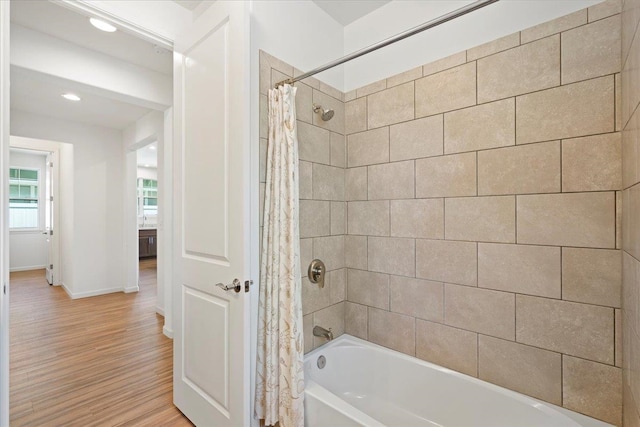 bathroom featuring baseboards, wood finished floors, shower / bath combo, and recessed lighting