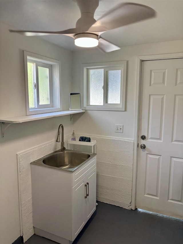 kitchen featuring ceiling fan, wainscoting, white cabinets, tile walls, and a sink