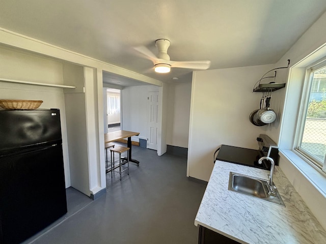 kitchen featuring finished concrete flooring, ceiling fan, freestanding refrigerator, stove, and a sink