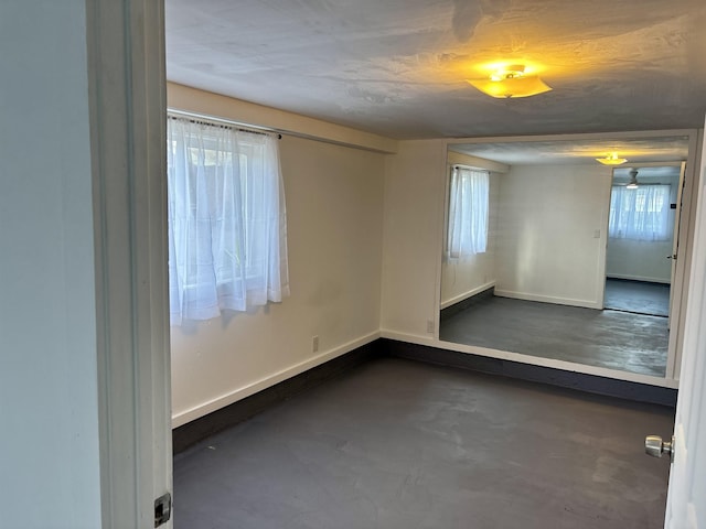 unfurnished room featuring a wealth of natural light, concrete floors, and baseboards