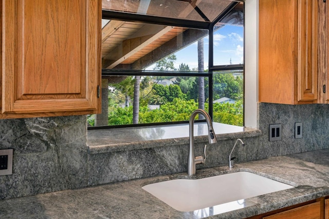 kitchen featuring decorative backsplash, brown cabinets, dark stone counters, and a sink