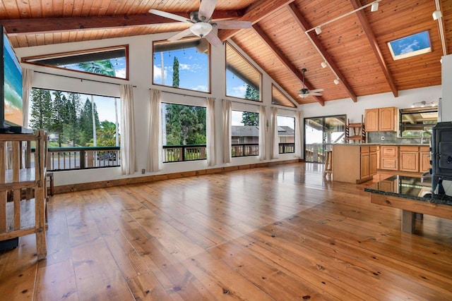 living area featuring beam ceiling, light wood-style flooring, wooden ceiling, a wood stove, and high vaulted ceiling