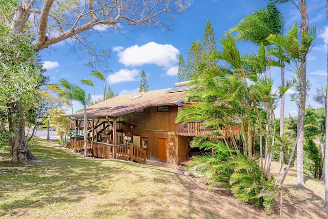 back of property featuring a yard, roof mounted solar panels, and a deck