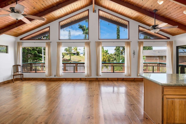 unfurnished living room with beam ceiling, a healthy amount of sunlight, hardwood / wood-style floors, and a ceiling fan