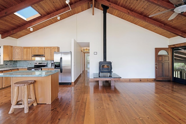 kitchen featuring hardwood / wood-style floors, a wood stove, stainless steel appliances, decorative backsplash, and a center island