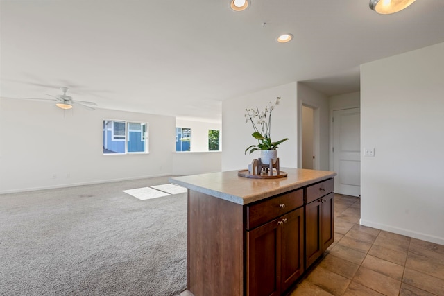 kitchen featuring ceiling fan, a center island, light colored carpet, and dark brown cabinets