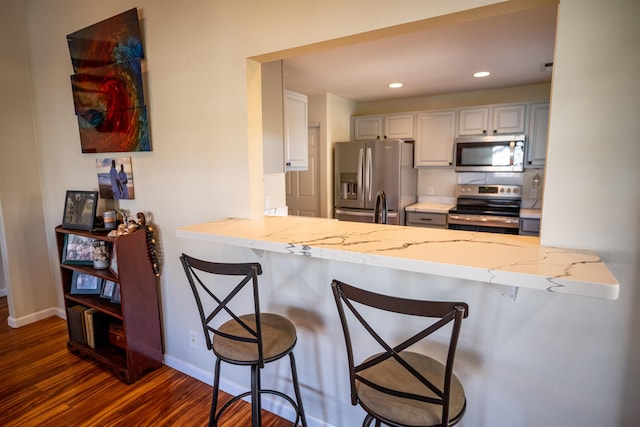 kitchen with appliances with stainless steel finishes, a breakfast bar, white cabinets, and kitchen peninsula