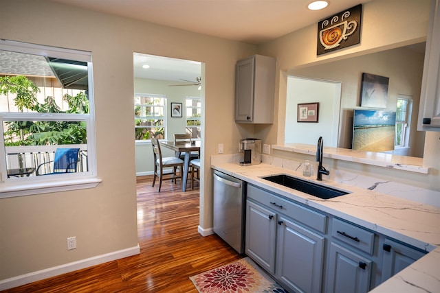 kitchen with gray cabinets, dark hardwood / wood-style floors, sink, stainless steel dishwasher, and light stone countertops