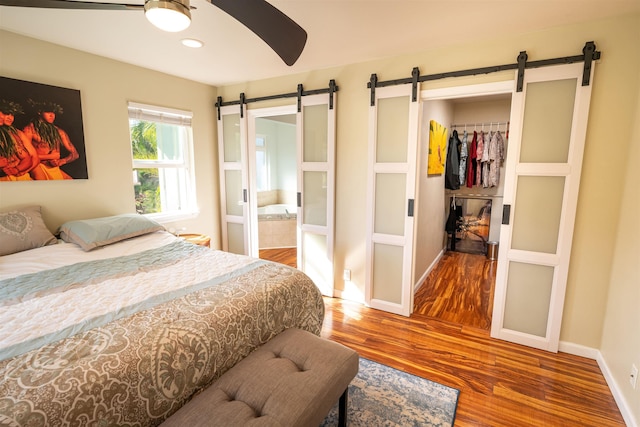 bedroom featuring connected bathroom, wood-type flooring, a closet, ceiling fan, and a barn door