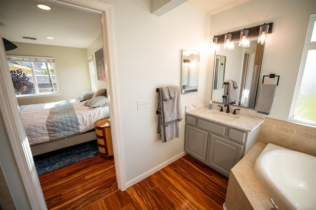 bathroom with hardwood / wood-style flooring, vanity, and a relaxing tiled tub