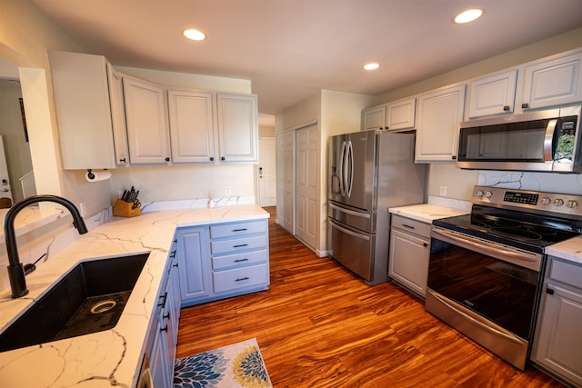 kitchen featuring sink, white cabinetry, light stone counters, light hardwood / wood-style flooring, and stainless steel appliances