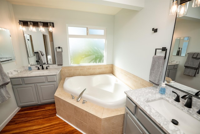 bathroom with vanity, tiled tub, and wood-type flooring