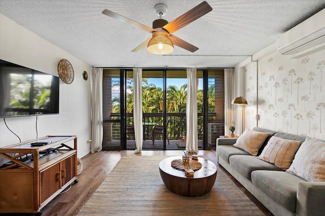 living area featuring an AC wall unit, a textured ceiling, ceiling fan, floor to ceiling windows, and wood finished floors