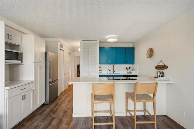 kitchen with stainless steel appliances, a sink, a peninsula, a kitchen breakfast bar, and dark wood finished floors