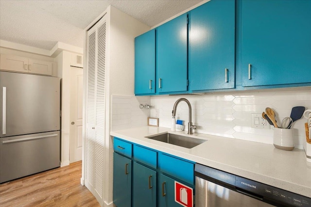 kitchen with appliances with stainless steel finishes, a sink, a textured ceiling, light countertops, and light wood finished floors