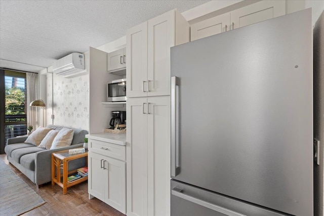 kitchen with appliances with stainless steel finishes, a wall mounted air conditioner, a textured ceiling, wood finished floors, and light countertops