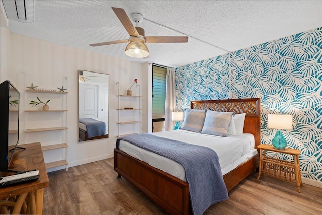 bedroom featuring wallpapered walls, wood finished floors, a textured ceiling, ceiling fan, and baseboards