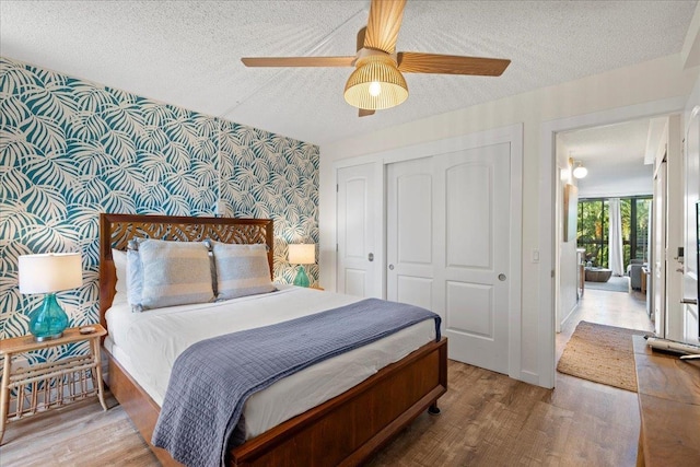 bedroom featuring wallpapered walls, a textured ceiling, a closet, wood finished floors, and an accent wall