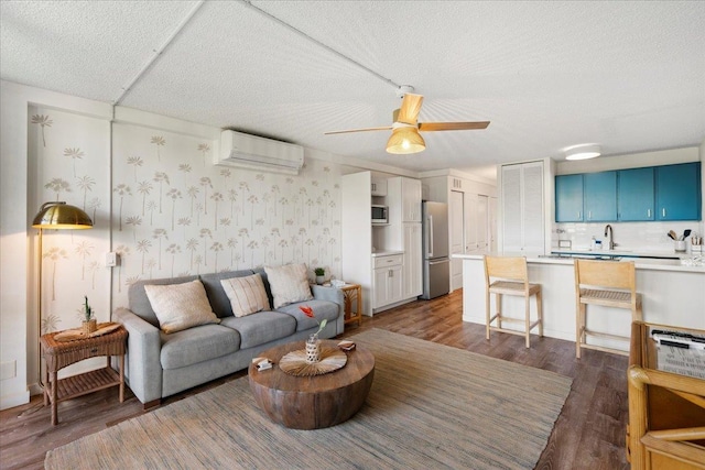 living room featuring wood finished floors, an AC wall unit, ceiling fan, and a textured ceiling