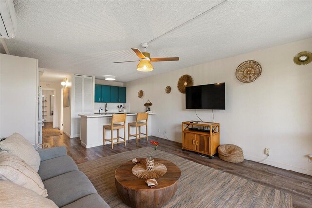 living area featuring wood finished floors, a ceiling fan, a textured ceiling, and baseboards