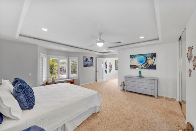 bedroom featuring ceiling fan, a raised ceiling, and light carpet