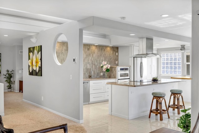 kitchen with appliances with stainless steel finishes, exhaust hood, white cabinetry, kitchen peninsula, and a breakfast bar