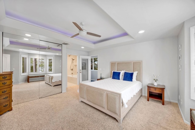 bedroom featuring ceiling fan, ensuite bathroom, light colored carpet, and a tray ceiling