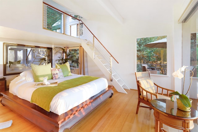 bedroom featuring beam ceiling, light wood-type flooring, and a high ceiling