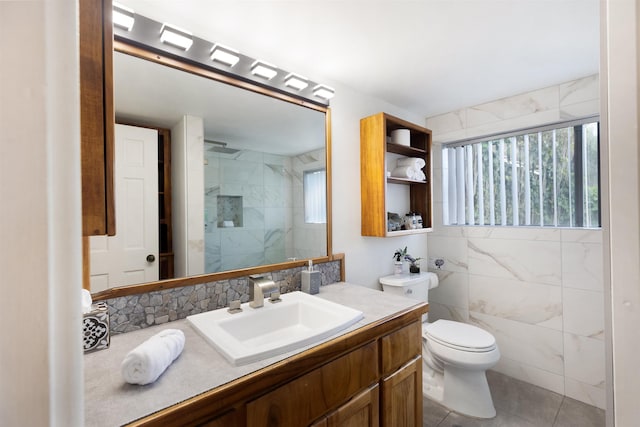 bathroom featuring a tile shower, vanity, tile walls, tile patterned flooring, and toilet