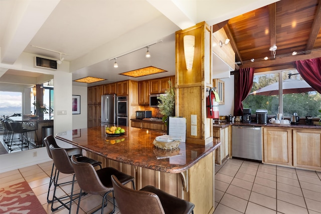 kitchen featuring a healthy amount of sunlight, dark stone countertops, appliances with stainless steel finishes, light tile patterned flooring, and wood ceiling