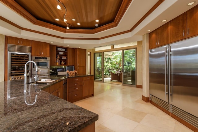 kitchen featuring appliances with stainless steel finishes, ornamental molding, a tray ceiling, sink, and dark stone countertops