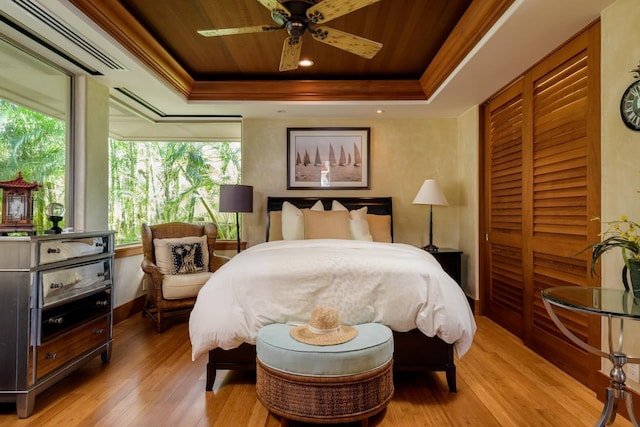 bedroom featuring ceiling fan, light wood-type flooring, multiple windows, and a tray ceiling