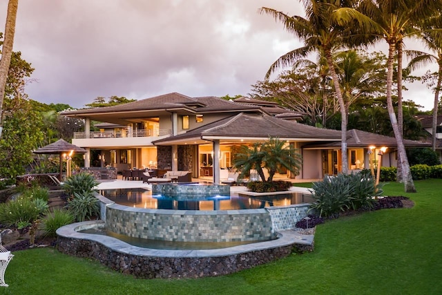 back house at dusk featuring a lawn, outdoor lounge area, pool water feature, a balcony, and a patio area