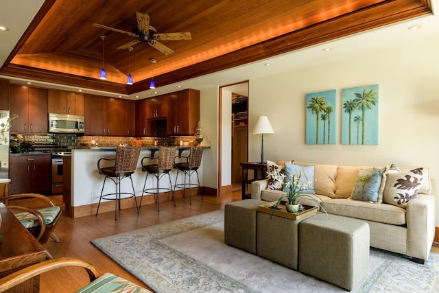 living room featuring light hardwood / wood-style floors, a raised ceiling, ceiling fan, and wood ceiling