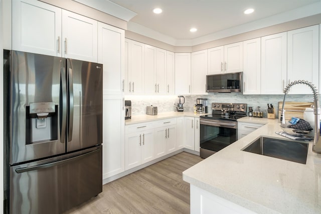 kitchen featuring appliances with stainless steel finishes, tasteful backsplash, white cabinets, light hardwood / wood-style flooring, and sink