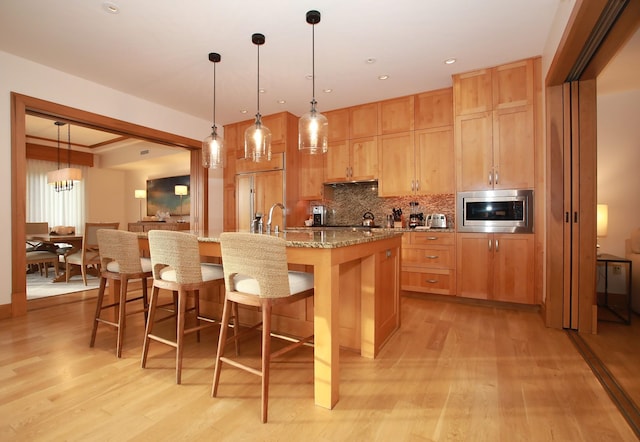 kitchen with light hardwood / wood-style flooring, an island with sink, built in appliances, stone counters, and a breakfast bar