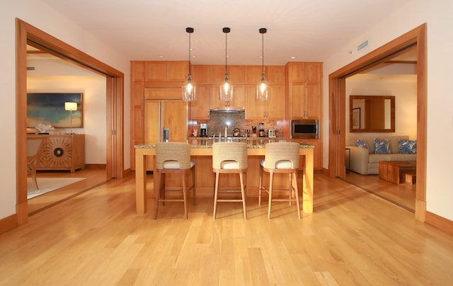 kitchen featuring light hardwood / wood-style flooring, a kitchen breakfast bar, hanging light fixtures, a center island with sink, and built in appliances