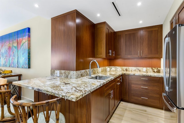 kitchen with stainless steel fridge, light stone countertops, and kitchen peninsula