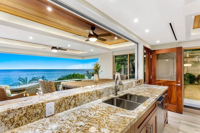 kitchen with a raised ceiling, a water view, light wood-type flooring, and sink