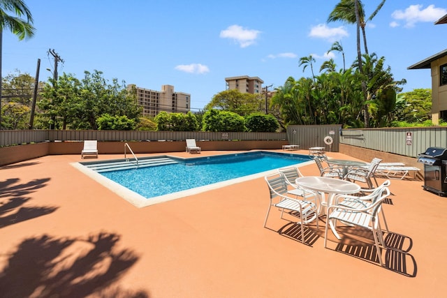 pool with grilling area, a patio area, and fence
