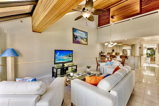 living room with ceiling fan with notable chandelier, baseboards, a high ceiling, and light tile patterned floors