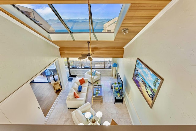 living room with a towering ceiling, tile patterned floors, a ceiling fan, a skylight, and a sunroom