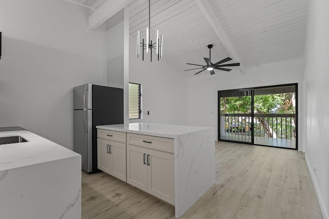 kitchen featuring vaulted ceiling with beams, light stone countertops, light wood-type flooring, freestanding refrigerator, and white cabinetry