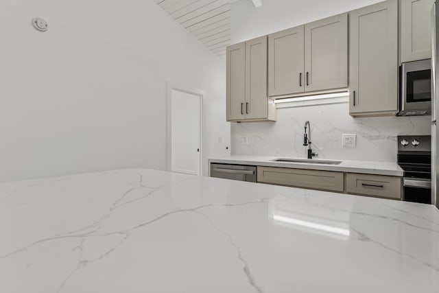 kitchen featuring light stone countertops, gray cabinets, a sink, appliances with stainless steel finishes, and tasteful backsplash