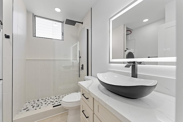 bathroom featuring vanity, washer / clothes dryer, recessed lighting, a tile shower, and toilet