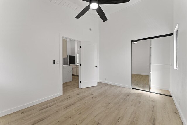 unfurnished bedroom with a ceiling fan, light wood-style floors, baseboards, and high vaulted ceiling