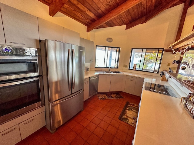 kitchen with sink, dark tile patterned floors, appliances with stainless steel finishes, vaulted ceiling with beams, and wooden ceiling