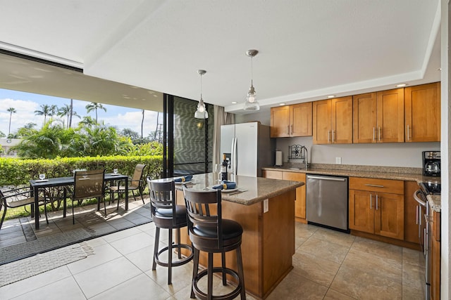 kitchen with stainless steel appliances, brown cabinetry, a kitchen island, and light tile patterned floors