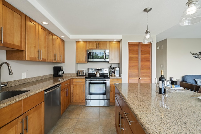 kitchen with recessed lighting, a sink, appliances with stainless steel finishes, light stone countertops, and brown cabinetry